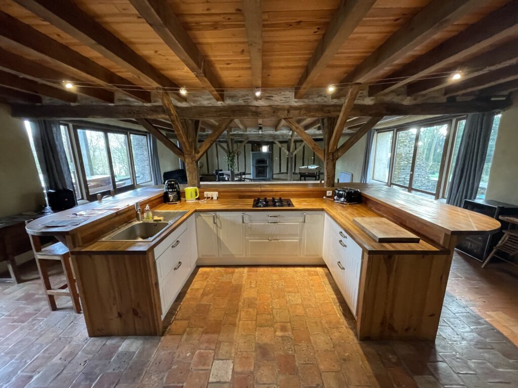 Cuisine en U en bois sous les poutres, ouverte sur la salle
