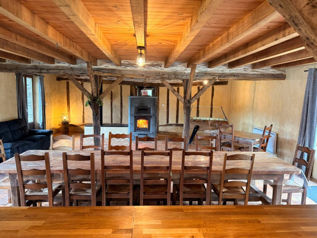 La grande table de la pièce de vie sous les poutres, poêle de masse au fond