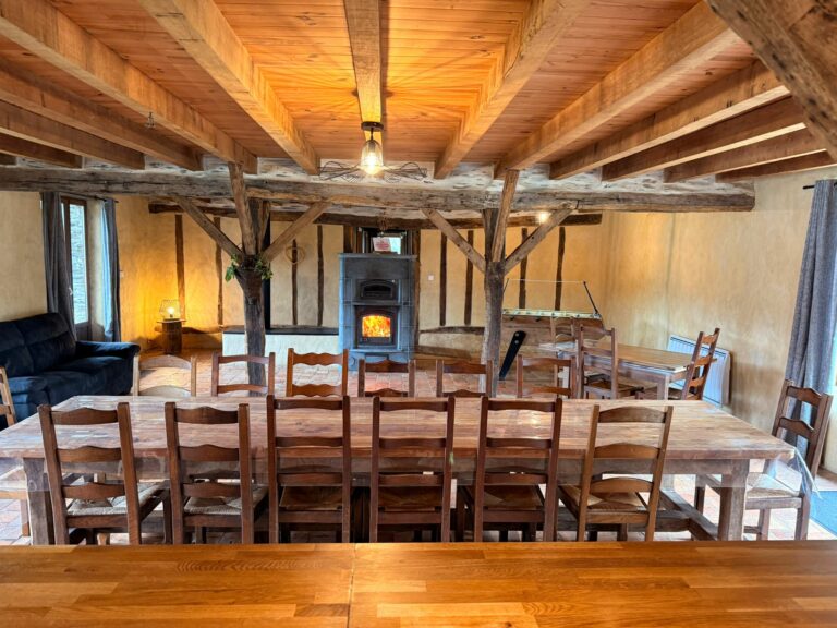 Pièce de vie de 100 m² : grande table sous la charpente et poêle de masse